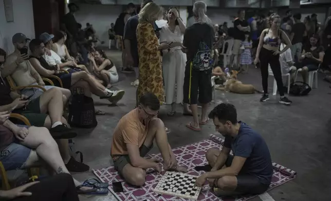 People take shelter as air raid sirens warn of incoming Iranian strikes in Tel Aviv, Israel, Friday, June 20, 2025. (AP Photo/Leo Correa)