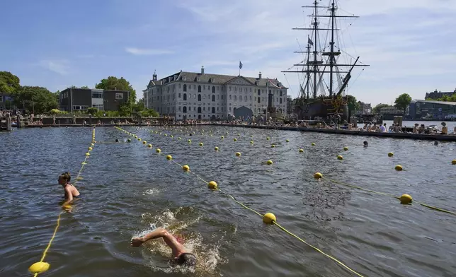 With temperatures soaring people swim in the harbour near the Maritime Museum, rear, in Amsterdam, Netherlands, Friday, June 20, 2025. (AP Photo/Peter Dejong)