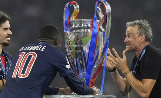 PSG's head coach Luis Enrique and players Vitinha, left, and Ousmane Dembele look at the trophy at the end of the Champions League final soccer match between Paris Saint-Germain and Inter Milan at the Allianz Arena in Munich, Germany, Saturday, May 31, 2025. (AP Photo/Luca Bruno
