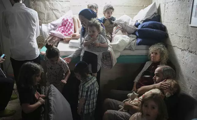 Israelis take shelter in a basement as a siren sounds a warning following missile launches from Iran, in Jerusalem, Sunday, June 15, 2025. (AP Photo/Ohad Zwigenberg)