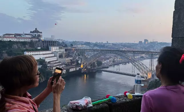 People rest their plastic hammers on a wall while watching flying lanterns soaring above the Douro river as the northern Portugal city of Porto, gears up to celebrate Saint John feast, Monday evening, June 23, 2025. (AP Photo/Helena Alves)