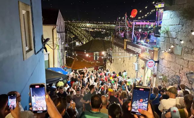 People cheer and shoot video of a group releasing a flying lantern while celebrating the Saint John feast by the the Douro river in Porto, northern Portugal, Monday night, June 23, 2025. (AP Photo/Helena Alves)