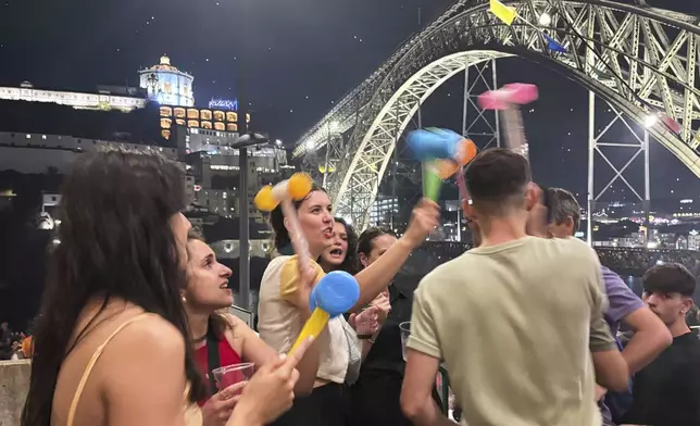 Young people use their plastic hammers on each other while celebrating the Saint John feast by the the Douro river in Porto, northern Portugal, Monday night, June 23, 2025. (AP Photo/Helena Alves)