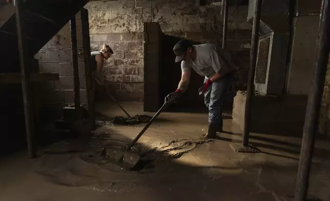 Emily Kolence, left, and Connoor Crowe, right, shovel the thick, muddy floodwaters as they look for belongings in John Gearry's flooded basement, Monday, June 16, 2025, in Valley Grove, W.Va. (AP Photo/Carolyn Kaster)