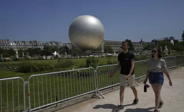 People walk past the Olympic cauldron at the Tuileries Gardens, ahead of its nightly summer relaunch starting June 21, in Paris, Thursday, June 12, 2025. (AP Photo/Michel Euler)