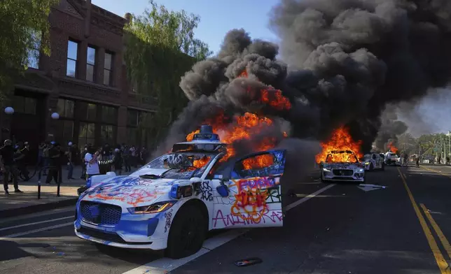 FILE - Multiple Waymo taxis burn near the Metropolitan Detention Center of downtown Los Angeles, Sunday, June 8, 2025, following last night's immigration raid protest. (AP Photo/Eric Thayer, File)