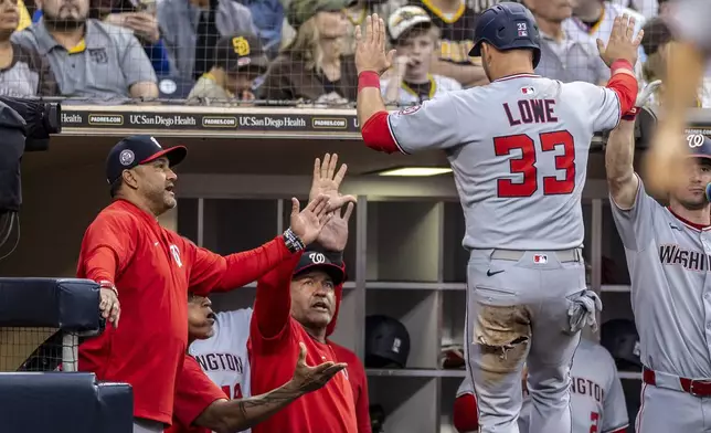 Washington Nationals manager Dave Martinez, left, gives a hand to Nathaniel Lowe (33) after Lowe scored off a Brady House single in the fourth inning of a baseball game against the San Diego Padres, Monday, June 23, 2025, in San Diego. (AP Photo/Tony Ding)