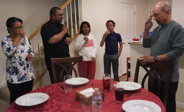 The Rev. Ricky Malebranche, second from left, makes the sign of the cross as he leads prayers before a family meal at his home in Gainesville, Va., on Sunday, May 25, 2025. (AP Photo/Luis Andres Henao)