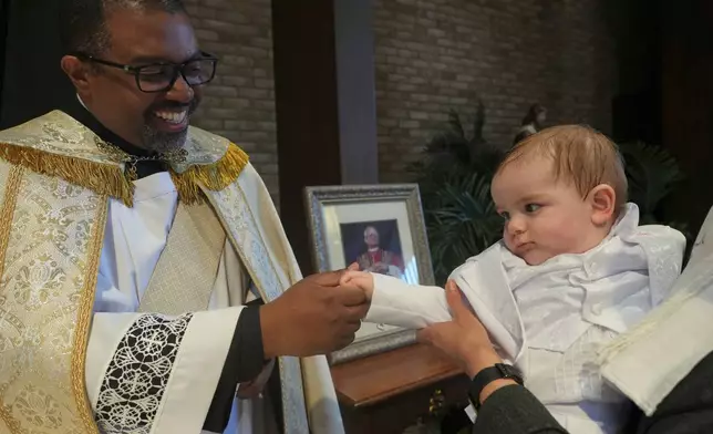 The Rev. Ricky Malebranche holds the hand of 9-month-old Andres Roman Marquez after baptizing him at St. Louis Catholic Church in Alexandria, Va., on Saturday, May 24, 2025. (AP Photo/Luis Andres Henao)