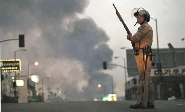 FILE - A California Highway Patrol officer stands guard at Ninth Street and Vermont Avenue in Los Angeles as smoke rises from a fire further down the street, April 30, 1992. (AP Photo/David Longstreath, file)