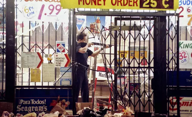FILE - In this April 30, 1992 file photo, a Los Angeles police officer takes aim at a looter in a market at Alvarado and Beverly Boulevard in Los Angeles during the second night of rioting in the city. (AP Photo/John Gaps III, File)