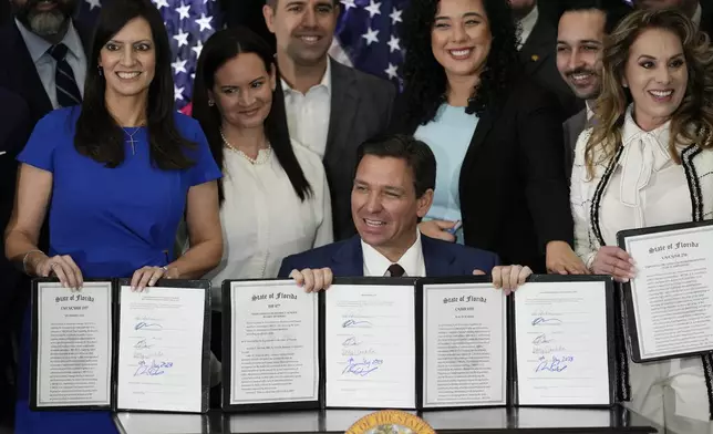 FILE - Florida Governor Ron DeSantis, seated, and other elected, state, and local officials pose with a group of education-related bills after DeSantis signed them into law at a press conference in Miami, Tuesday, May 9, 2023. (AP Photo/Rebecca Blackwell, File)