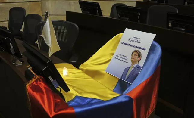 A picture of Colombian Senator Miguel Uribe Turbay and Colombian flag cover his seat at Congress while he is in critical condition after being shot at a political rally in Bogota, Colombia, Monday, June 9, 2025. (AP Photo/Ivan Valencia)