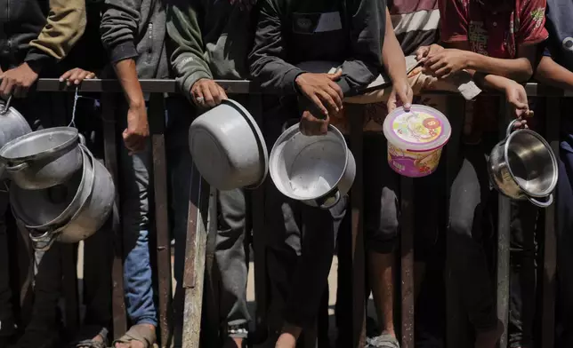 Holding their pots, Palestinians wait to get donated food at a community kitchen in Khan Younis, southern Gaza Strip, Monday, June 2, 2025. (AP Photo/Abdel Kareem Hana)