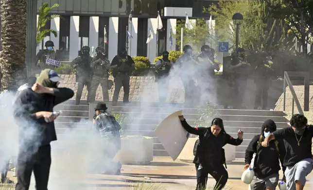 Protesters run from police as they use tear gas and flash-bangs at the Federal Building in Santa Ana, Calif., on Monday, June 9, 2025. (Jeff Gritchen/The Orange County Register via AP)