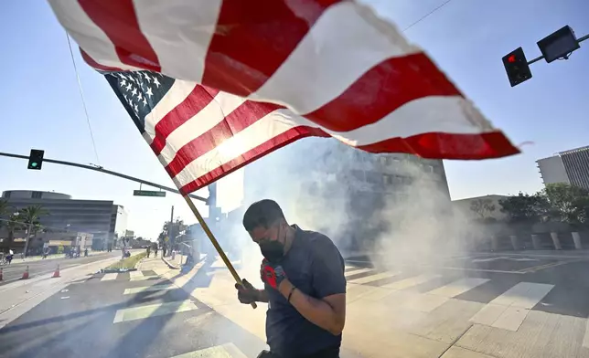 A protester raises the U.S. flag after police use tear gas and flash-bangs at the Federal Building in Santa Ana, Calif., on Monday, June 9, 2025. (Jeff Gritchen/The Orange County Register via AP)