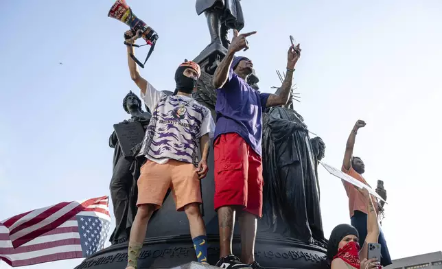 Protesters cheer from pedestal of a statue during a protest against Immigration and Customs Enforcement and the Trump administration at Metro Hall, Monday, June 9, 2025, in Louisville, Ky. (AP Photo/Jon Cherry)