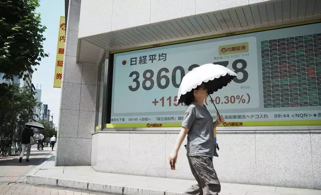 A person walks in front of an electronic stock board showing Japan's Nikkei index at a securities firm Friday, June 20, 2025, in Tokyo. (AP Photo/Eugene Hoshiko)