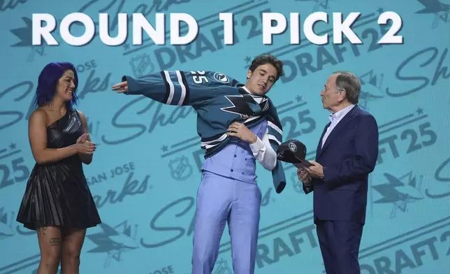 Michael Misa, middle, puts on a jersey between WWE wrestler Bayley, left, and NHL commissioner Gary Bettman after being drafted by the San Jose Sharks during the NHL hockey draft Friday, June 27, 2025, in Los Angeles. (AP Photo/Damian Dovarganes)