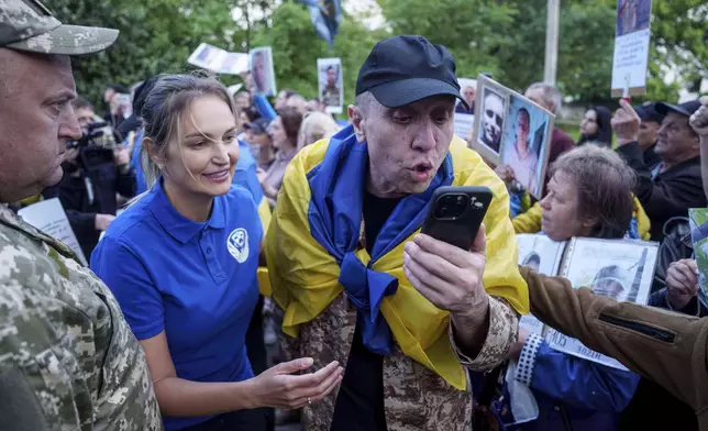 A Ukrainian soldier speaks to a relative on a phone as he is walking through a human corridor of people holding photos of their missed relatives after returning from captivity after a POWs exchange between Russia and Ukraine, in Chernyhiv region, Ukraine, Thursday, June 26, 2025. (AP Photo/Evgeniy Maloletka)