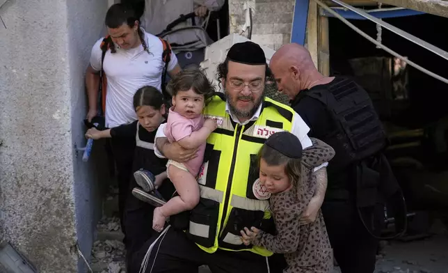 A rescue worker carries two children as residents evacuate from the site where a missile launched from Iran struck Haifa, Israel, Sunday, June 22, 2025. (AP Photo/Baz Ratner)