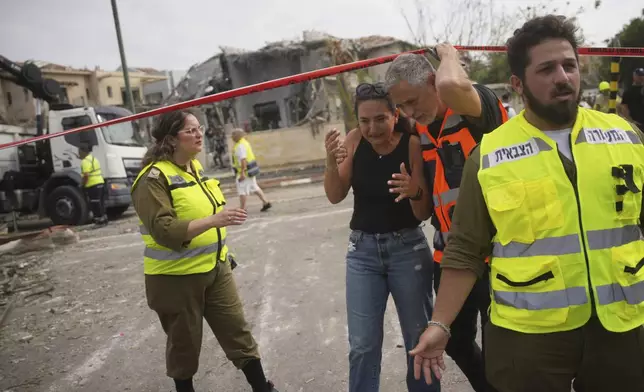 A rescue worker evacuates a woman from the site where a missile launched from Iran struck in Nes Ziona ,Israel, Sunday, June 22, 2025. (AP Photo/Ohad Zwigenberg)