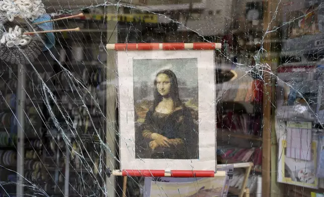 A poster of the Mona Lisa hangs in a shattered storefront window at the site where a missile launched from Iran struck in Haifa, Israel, Sunday, June 22, 2025. (AP Photo/Baz Ratner)