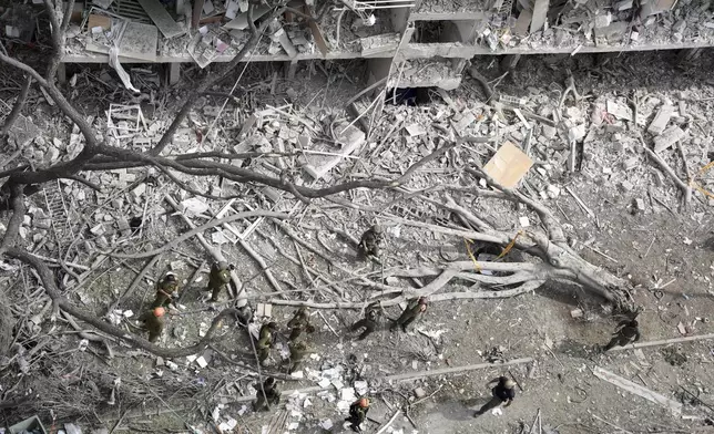 A torn-out tree lies among the rubble as firefighters, rescue workers, and military personnel survey the site of a direct missile strike launched from Iran in Tel Aviv, Israel, Sunday, June 22, 2025. (AP Photo/Oded Balilty)