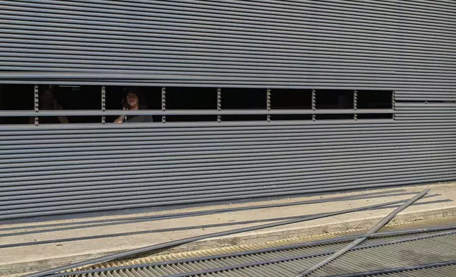 A woman looks through a hole in a partially damaged metal wall near the site of a direct missile strike launched from Iran, in Tel Aviv, Israel, Sunday, June 22, 2025. (AP Photo/Bernat Armangue)