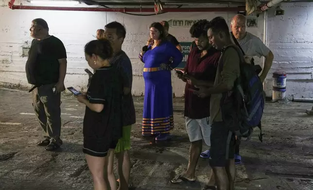 Residents check their cell phones at a shelter during an alarm for incoming missiles launched from Iran in Haifa, Israel, Sunday, June 22, 2025. (AP Photo/Baz Ratner)