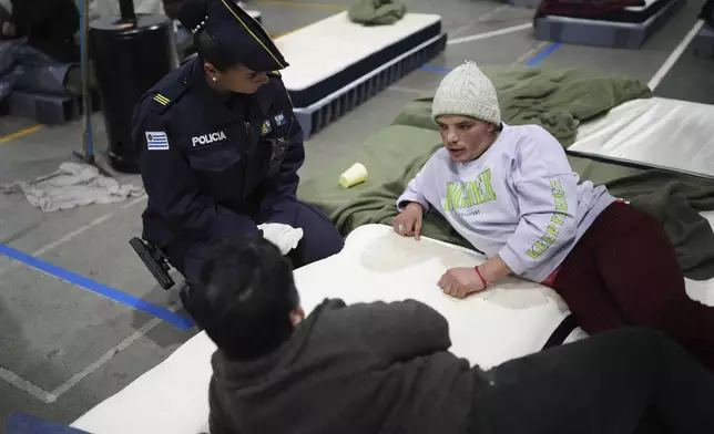 Camila Alvarez talks with a police officer at a gymnasium the government is using as a makeshift shelter in an effort to protect people without homes from cold weather in Montevideo, Uruguay, Wednesday, June 25, 2025. (AP Photo/Matilde Campodonico)