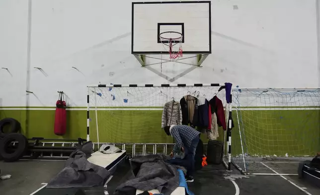 A person gets ready for bed at a gymnasium the government is using as a makeshift shelter in an effort to protect people without homes from cold weather in Montevideo, Uruguay, Wednesday, June 25, 2025. (AP Photo/Matilde Campodonico)