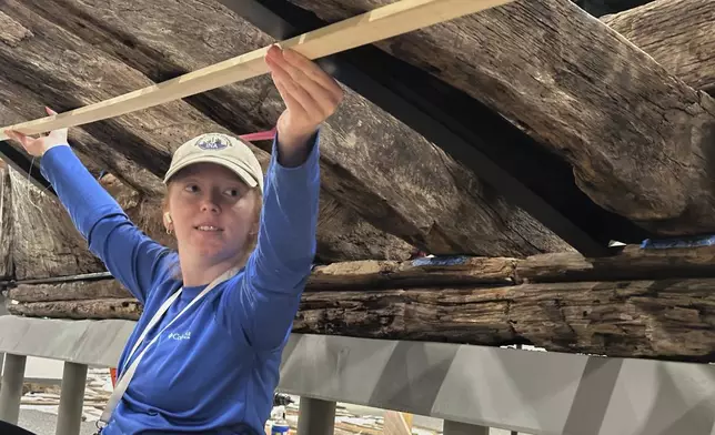 Research assistant Alyssa Carpenter works beneath a wooden Revolutionary War-era gunboat to prepare for the craft's partial reconstruction at the New York State Museum, Friday, May 30, 2025, in Albany, New York. (AP Photo/Michael Hill)