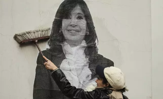 A supporter of Argentina's former President Cristina Fernandez uses a boom to paste a photo of her on the wall outside her home after the nation's Supreme Court upheld Fernandez's corruption conviction in Buenos Aires, Argentina, Tuesday, June 17, 2025. (AP Photo/Natacha Pisarenko)