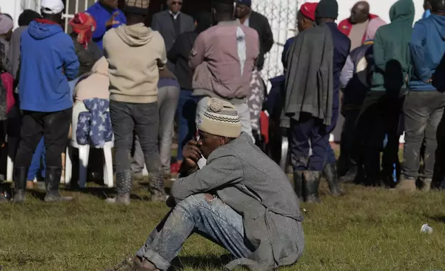 A man sits on the ground as a minister addresses flood victims outside a temporary shelter at a church following floodsin Mthatha, South Africa, Thursday, June 12, 2025. (AP Photo/Themba Hadebe)