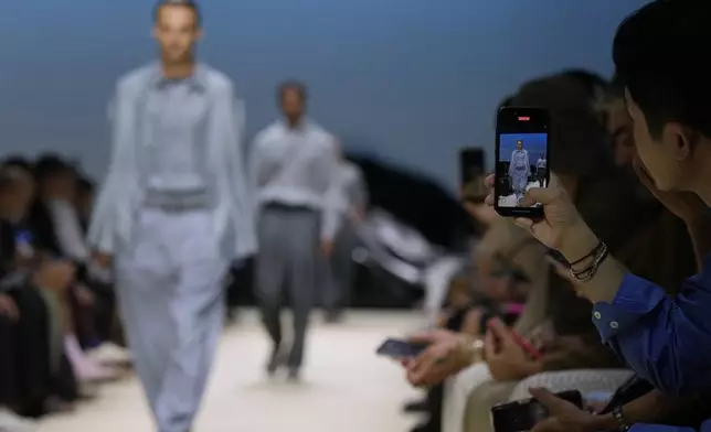A guest takes a photograph during the men's Giorgio Armani Spring-Summer 2026 collection, that was presented in Milan, Italy, Monday, June 23, 2025. (AP Photo/Luca Bruno)