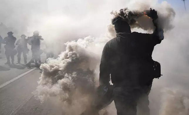 A protester throws a smoke canister on the 101 Freeway near the Metropolitan Detention Center of downtown Los Angeles, Sunday, June 8, 2025, following last night's immigration raid protest. (AP Photo/Eric Thayer)