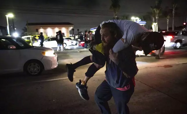 A person carries an injured protester to cover during a protest in Compton, Calif., Saturday, June 7, 2025, after federal immigration authorities conducted operations. (AP Photo/Ethan Swope)