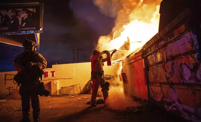 A law enforcement officer works to put out a fire during a protest in Compton, Calif., Saturday, June 7, 2025, after federal immigration authorities conducted operations. (AP Photo/Ethan Swope)