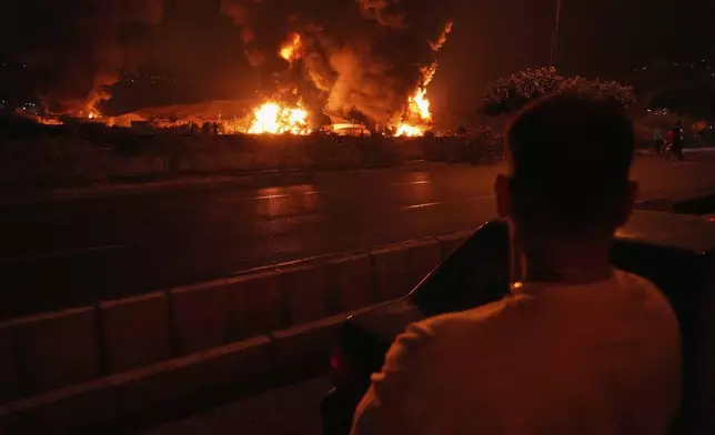 A man looks at flames rising from an oil storage facility after it appeared to have been struck by an Israeli strike in Tehran, Iran, early Sunday, June 15, 2025. (AP Photo/Vahid Salemi)