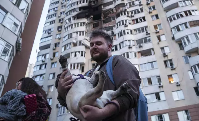 A man carries his dog in front of a residential multi-storey building damaged after a Russian drone strike on Kyiv, Ukraine, on Friday, June 6, 2025. (AP Photo/Evgeniy Maloletka)