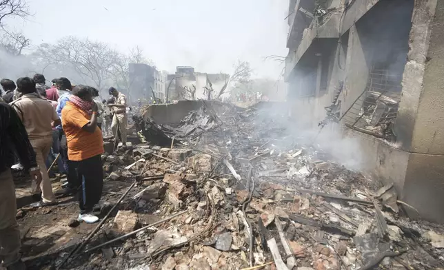 People stand around debris at the site of an airplane that crashed in India's northwestern city of Ahmedabad in Gujarat state, Thursday, June12, 2025. (AP Photo/Ajit Solanki)