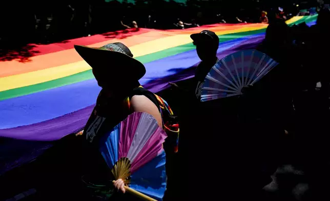FILE - Mac Weatherill, left, and Yexara Colón Martinez, second from left, hold transgender pride fans as they help carry a large rainbow flag on their fourth anniversary during the annual Seattle Pride Parade, June 25, 2023, in Seattle. (AP Photo/Lindsey Wasson)