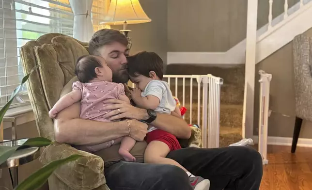 U.S. Marine Corps veteran Adrian Clouatre holds his 3-month-old daughter Lyn and his nearly two old son Noah at their home in Baton Rouge, La. on Tuesday, June 17, 2025. (AP Photo/Stephen Smith)