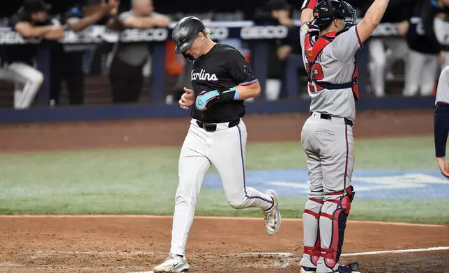Miami Marlins' Kyle Stowers, left, scores as Atlanta Braves catcher Sean Murphy, right, signals during the sixth inning of a baseball game, Friday, June 20, 2025, in Miami. (AP Photo/Michael Laughlin)