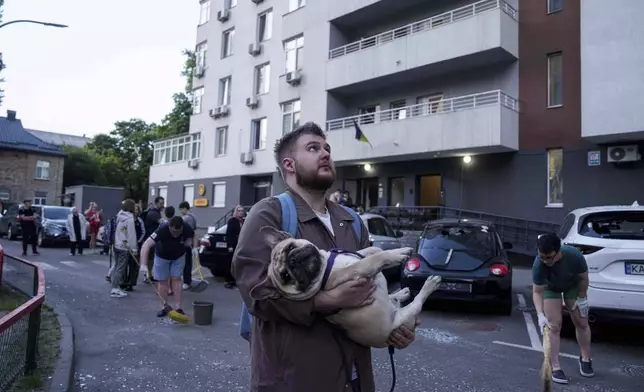 A man carries his dog in front of a residential multi-storey building damaged after a Russian drone strike on Kyiv, Ukraine, on Friday, June 6, 2025. (AP Photo/Evgeniy Maloletka)