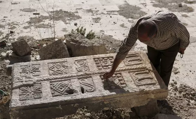 A guard inspects an engraved stone, originally found at a Byzantine underground tomb complex believed to be over 1,500 years old and uncovered by a contractor during the reconstruction of a war-damaged house and brought to a museum yard in Maarat al-Numan, Syria, Friday, May 30, 2025. (AP Photo/Omar Albam)