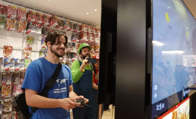 Darren Stallcup, left, of San Francisco reacts as Nicholas Oehlberg, right, of San Francisco documents the event as they play the Mario Kart World for Nintendo Switch 2 game with others at the Nintendo Store for a pre-launch event for the Ninentdo Switch 2 on Wednesday, June 4, 2025, in San Francisco. (Lea Suzuki/San Francisco Chronicle via AP)
