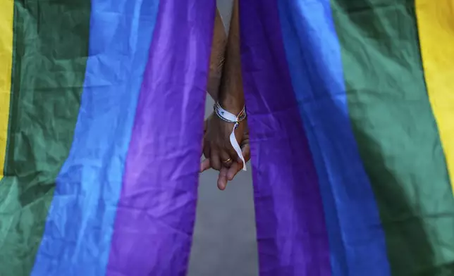 Two men wearing rainbow flags over their shoulders, walk hand-in-hand down Liberdade Avenue in Lisbon during the Europride Parade, Saturday, June 21, 2025. (AP Photo/Armando Franca)
