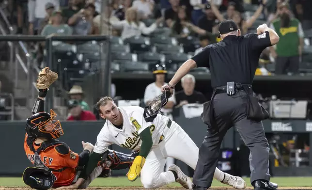 Baltimore Orioles catcher Maverick Handley, left, and Athletics' JJ Bleday (33) look to umpire Lance Barksdale for the call during the fifth inning of a baseball game Saturday, June 7, 2025, in West Sacramento, Calif. (AP Photo/Sara Nevis)